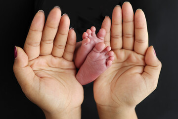 The palms of the parents. A mother hold the feet of a newborn child in a black blanket on a Black background. The feet of a newborn in the hands of parents. Photo of foot, heels and toes