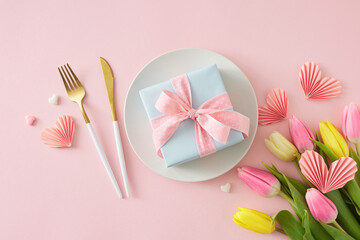 Mother's Day concept. Top view photo of circle plate and gift box cutlery knife fork bouquet of flowers yellow pink tulips and paper hearts on isolated pastel pink background