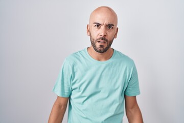 Obraz premium Middle age bald man standing over white background in shock face, looking skeptical and sarcastic, surprised with open mouth