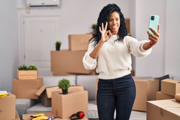 Fototapeta na wymiar Middle age hispanic woman moving to a new home taking selfie picture doing ok sign with fingers, smiling friendly gesturing excellent symbol