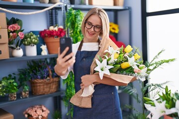 Young blonde woman florist make selfie by smartphone holding bouquet of flowers at florist shop