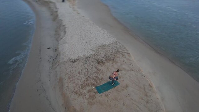A graceful yoga teacher is filmed by drone during her sunset session at the beach of Moliets in France, Europe