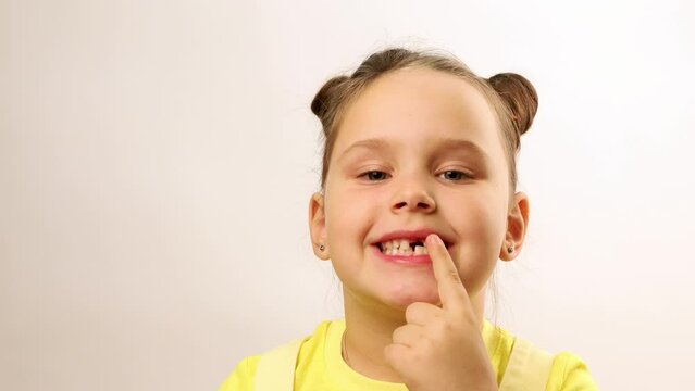 Little funny girl smile and emotionally point finger at gap in mouth from fallen tooth closeup, white background. Joyful toothless child show good result. Concept of healthy teeth and beautiful smile.