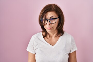 Middle age hispanic woman standing over pink background skeptic and nervous, frowning upset because of problem. negative person.