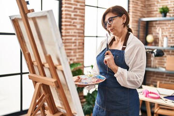 Middle age woman artist looking draw with doubt expression at art studio
