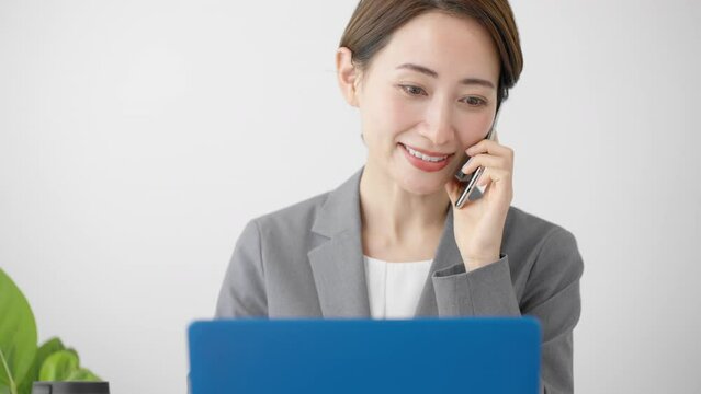 ノートパソコンを使いながらスマートフォンで通話をする若い女性　ビジネスイメージ	
