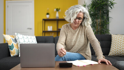 Middle age woman with grey hair writing on notebook accounting at home