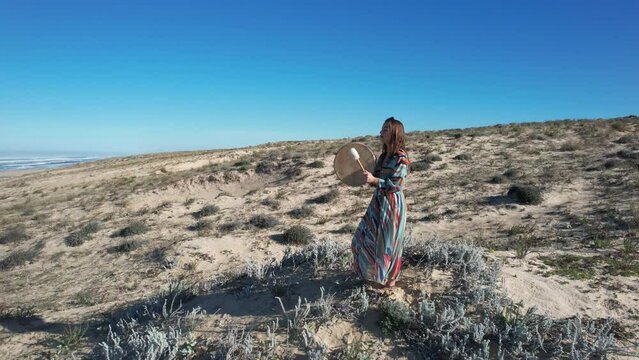 Beautiful woman in dress who plays the ceremonial drum while singing in front of the ocean