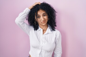 Hispanic woman with curly hair standing over pink background confuse and wondering about question....