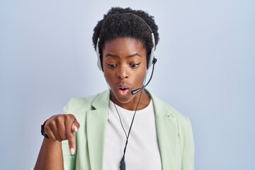 African american woman wearing call center agent headset pointing down with fingers showing advertisement, surprised face and open mouth