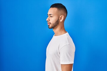 Young hispanic man standing over blue background looking to side, relax profile pose with natural face and confident smile.