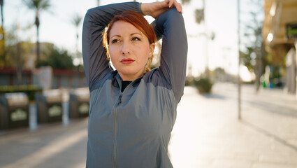 Young redhead woman wearing sportswear stretching at street