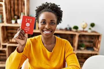 African american woman holding japan passport sitting on table at home