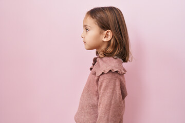 Little hispanic girl standing over pink background looking to side, relax profile pose with natural face with confident smile.