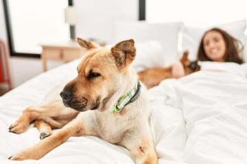 Young hispanic woman hugging dog lying on bed at bedroom