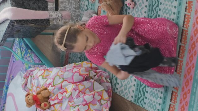 Vertical video. Little girl having fun in her messy room, throwing clothes up in the air