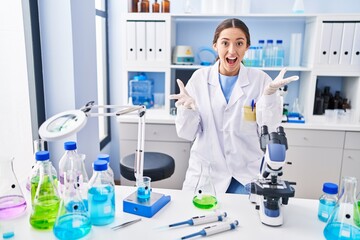 Fototapeta premium Young brunette woman working at scientist laboratory celebrating victory with happy smile and winner expression with raised hands