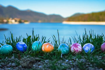 homemade painted natural eco easter eggs laying in the green grass infront of a bavarian mountain lake with blue water
