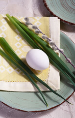 Easter table setting with green leaves, willow branch and white egg on green plate.
