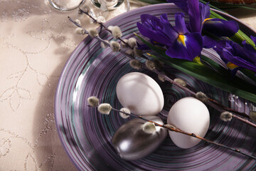 Easter table setting idea with violet iris flowers, willow branch and white and silver eggs on violet plate.