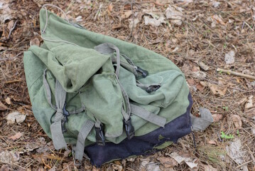 one empty old green black fabric backpack lies on gray dry grass in nature