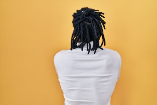 African man with dreadlocks wearing turtleneck sweater over yellow background standing backwards looking away with crossed arms