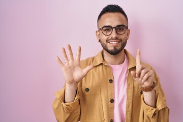 Young hispanic man standing over pink background showing and pointing up with fingers number six while smiling confident and happy.