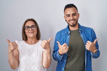 Hispanic mother and son standing together success sign doing positive gesture with hand, thumbs up smiling and happy. cheerful expression and winner gesture.