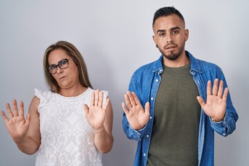 Hispanic mother and son standing together moving away hands palms showing refusal and denial with...