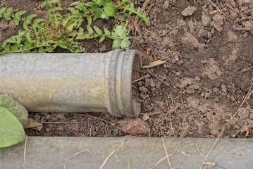 one gray metal sewer pipe lies on brown earth among green vegetation on the street
