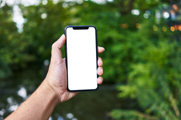 Man holding smartphone showing white blank screen at park - obrazy, fototapety, plakaty