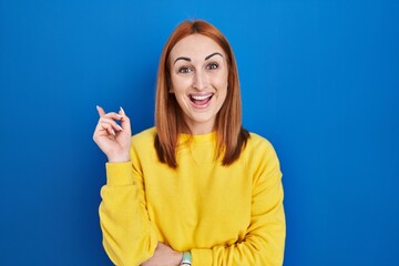 Fototapeta premium Young woman standing over blue background with a big smile on face, pointing with hand finger to the side looking at the camera.