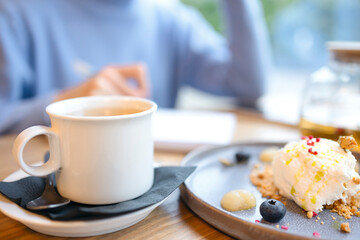 A white cup of tea, a cake on a blue plate, a girl in a blue sweater. A woman on a blurred background sits in a cafe and writes in a notebook, works remotely, writes a letter or a plan. freelancer