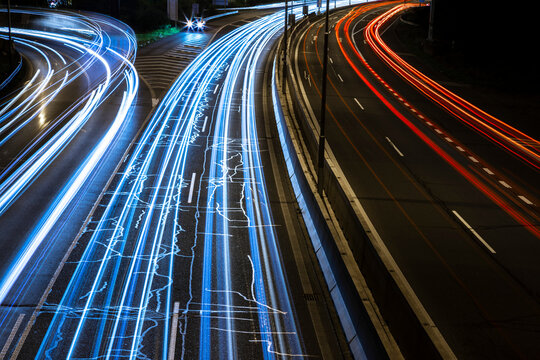 Lightlines of car headlights and rear lights captured by long exposure. Motorway in the city, stronger traffic in left line. Red lights in right, opposite direction. Patched cracks in the road
