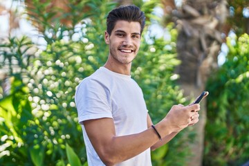 Naklejka na ściany i meble Young hispanic man smiling confident using smartphone at park