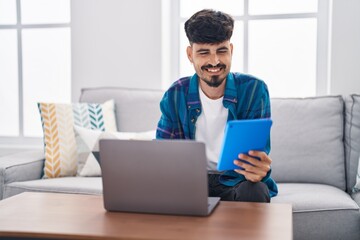 Young hispanic man using laptop and touchpad sitting on sofa at home