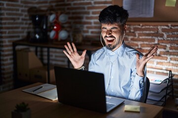 Young hispanic man with beard working at the office at night celebrating mad and crazy for success...