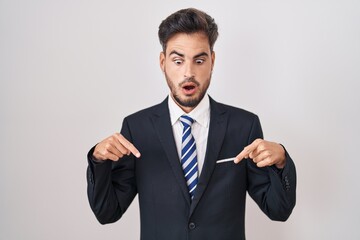 Young hispanic man with tattoos wearing business suit and tie pointing down with fingers showing advertisement, surprised face and open mouth