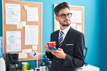 Young hispanic man business worker using smartphone drinking coffee at office