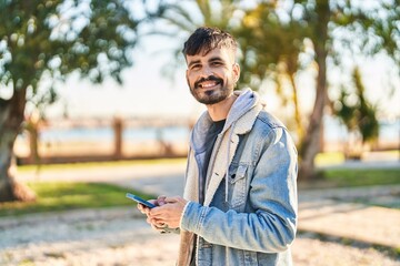 Young hispanic man smiling confident using smartphone at park