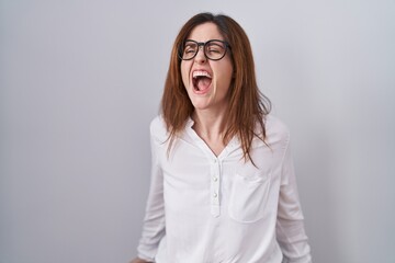 Brunette woman standing over white isolated background angry and mad screaming frustrated and furious, shouting with anger. rage and aggressive concept.