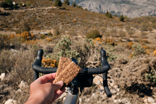 Cycling snack.Sports snack for cyclist.A sports bar in the hand of a cyclist against the background of a bicycle.Energy sports bar.