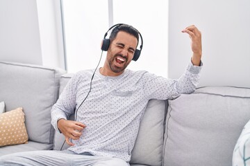 Young hispanic man listening to music doing guitar gesture at home