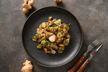 Roasted Jerusalem artichoke root, topinambur, sunchokes with parsley on brown background. View from above.