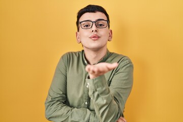 Obraz premium Non binary person standing over yellow background looking at the camera blowing a kiss with hand on air being lovely and sexy. love expression.
