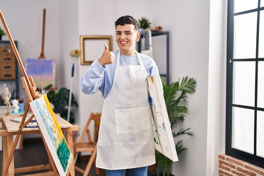 Non binary person at art studio smiling happy and positive, thumb up doing excellent and approval sign