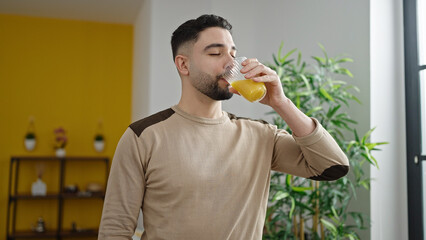 Young arab man drinking glass of orange juice at home