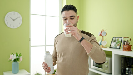 Young arab man drinking glass of milk standing at home