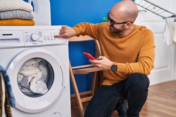 Young man using smartphone turning on washing machine at laundry room
