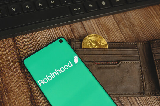 Robinhood app green logo with gold Bitcoin in a brown wallet and keyboard on wood background. WARSAW, POLAND - FEBRUARY 17, 2021